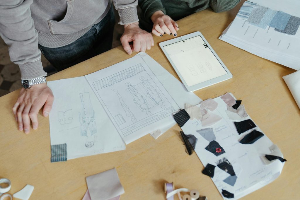 pexels-photo-4622224-4622224 Two designers examine clothing sketches and fabric swatches on a worktable, highlighting fashion creativity.